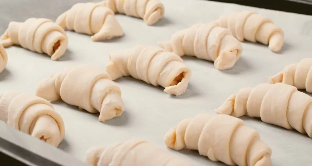 Raw croissants with filling prepared to be baked on the parchment. Making bakery products at home