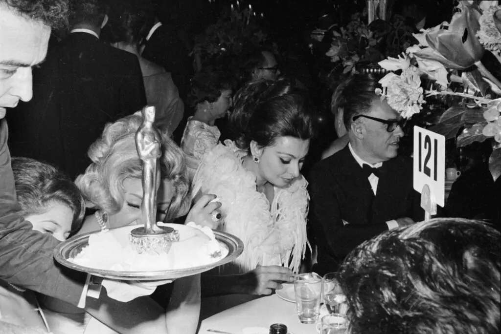 Italian-born actress Sophia Loren eats at the Academy Awards as a waiter walks by with an Oscar, Santa Monica, California, April 8, 1963. (Photo by Hulton Archive/Getty Images)