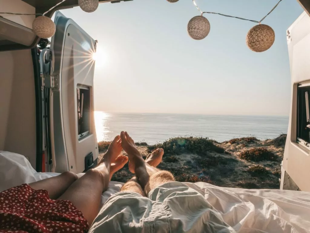 Road trip concept, couple living the van life experience watching stunning view while lying on the bed of the back of her camper