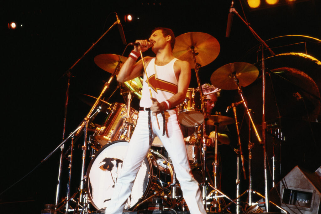 Freddie Mercury (1946-1991), singer with Queen, standing in front of a drumkit as he sings into a microphone on stage during a live concert performance by the band at the National Bowl in Milton Keynes, England, United Kingdom, on 5 June 1982. (Photo by Fox Photos/Hulton Archive/Getty Images)