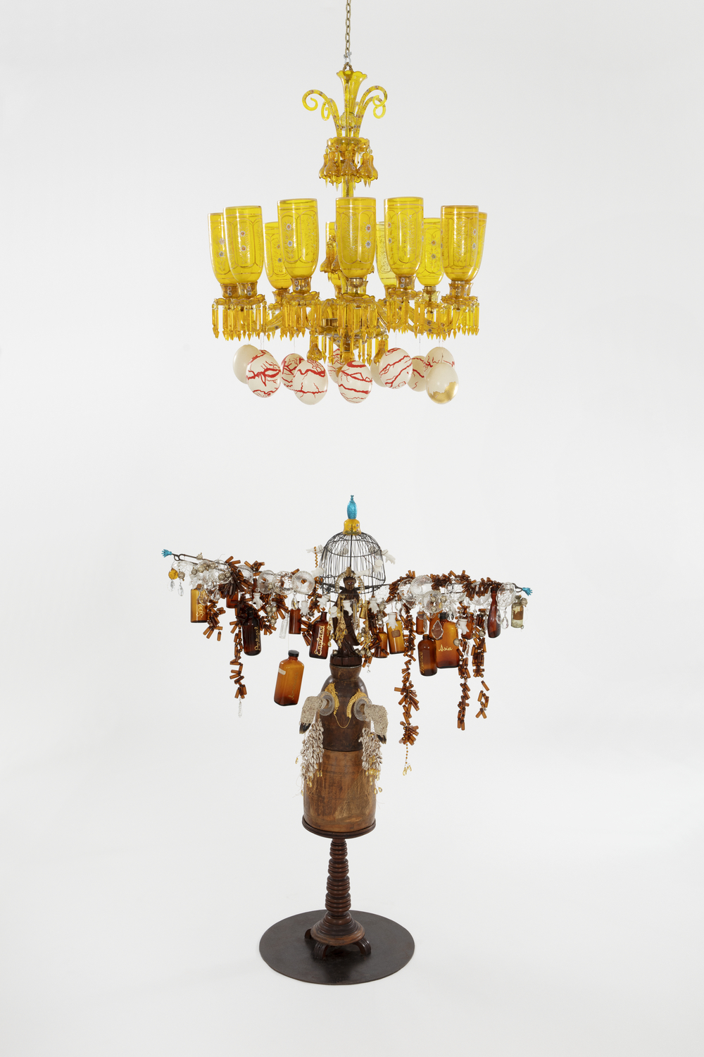 Rina Banerjee, Lady of Commerce, 2012; Hand-painted, leaded glass chandelier, wood figurine, vintage glass bottles, chandelier ornaments, birdcage, steel, wood pedestal, lace, cowry shells, taxidermy deer paws, Indian marriage jewelry, ostrich eggshells, porcelain doll hands, silver leaf, gold leaf, wire, linen cord, and marble baby doll hands, 120 x 48 in. diameter; Courtesy of the artist; © Rina Banerjee; Image courtesy of the artist and Perrotin; Photo by Guillaume Ziccarelli